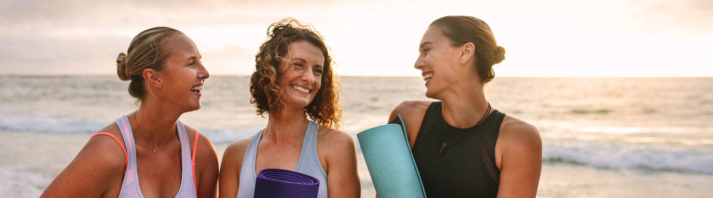 3 women carrying  yoga mat at beach